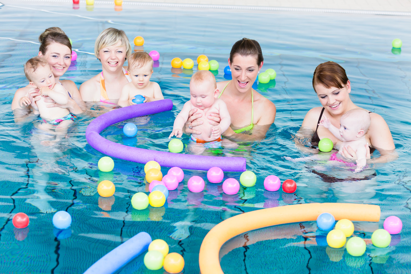 Moms and their newborns playing together with balls and pool noodles at infant swimming class